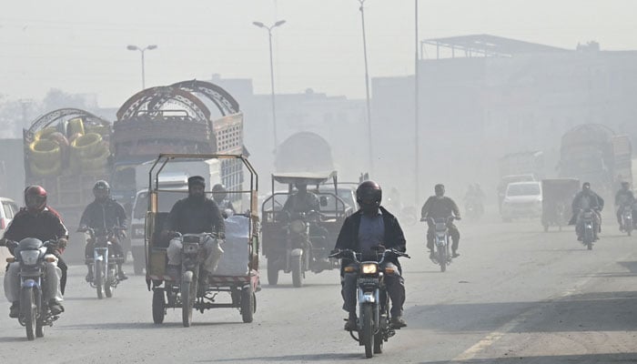 People commute along a road amid dense smog in Lahore on November 28, 2024. — AFP