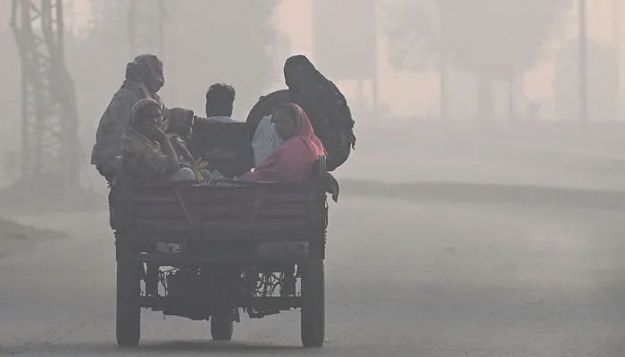 Commuters move along a road engulfed in smog in Lahore on November 21, 2024. — AFP