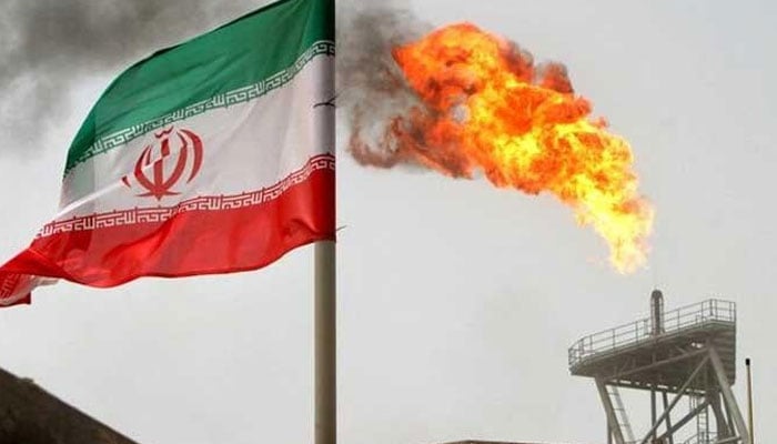 A gas flare on an oil production platform in the Soroush oil fields is seen alongside an Iranian flag in the Gulf July 25, 2005. — Reuters