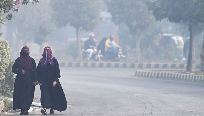 Women walk along a street amid dense smog in Lahore on November 29, 2024.— AFP