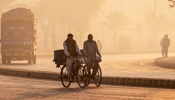 Vendors ride bicycles along a street engulfed in smog, in Lahore on December 1, 2024. — AFP