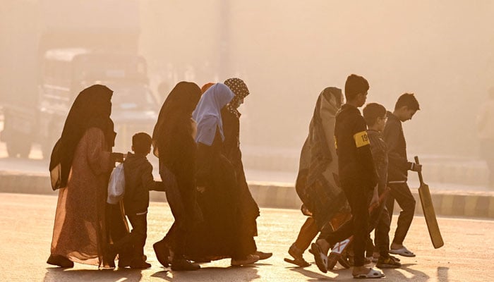 Women and children walk across a street engulfed in smog, in Lahore on December 1, 2024. — AFP