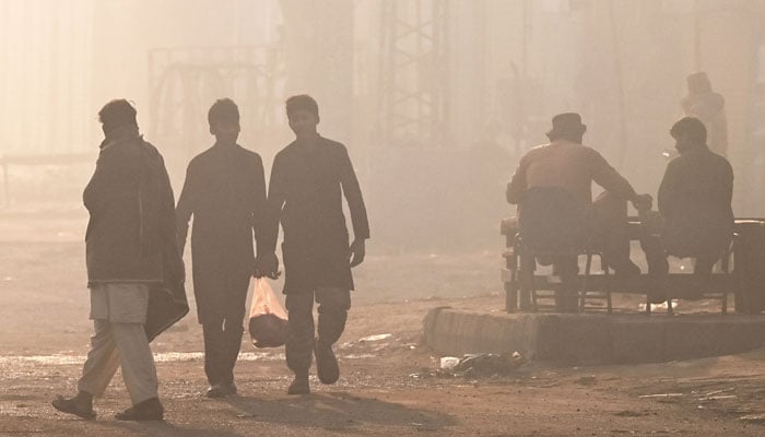 Men walk along a street engulfed in smog, in Lahore on December 2, 2024. — AFP