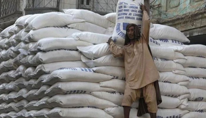 A labourer is pictured carrying a sugar bag with a large number of sugar bags stacked behind him. — AFP/File