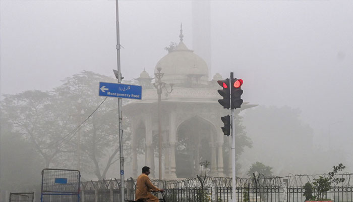 A man rides his bicycle along a street engulfed in smog in Lahore on November 14, 2024. — AFP