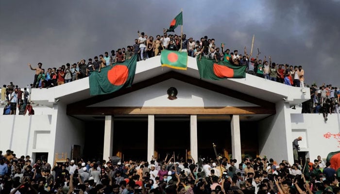 Anti-government protestors display Bangladeshs national flag as they storm Prime Minister Sheikh Hasinas palace in Dhaka on Aug 5, 2024. — AFP