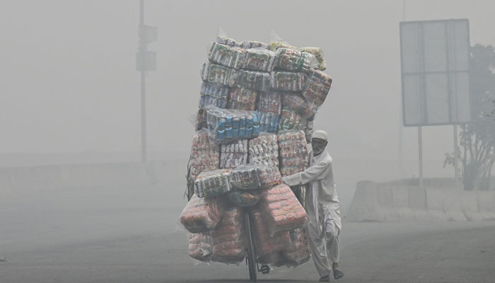 A vendor transports food items on his bicycle along a road engulfed in smog in Lahore on November 8, 2024. — AFP