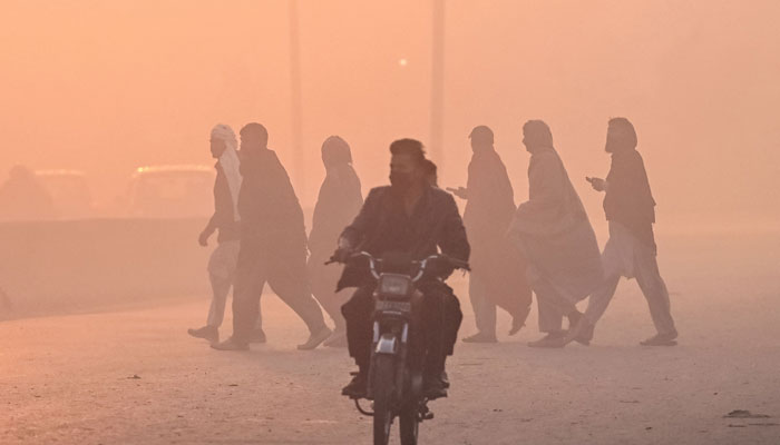 A man wearing a mask rides a motorbike along a street engulfed in smog, in Lahore on December 2, 2024. — AFP