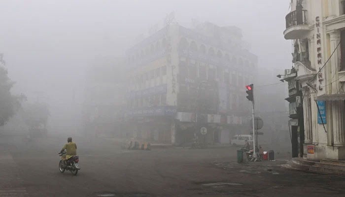 A man rides his motorbike along a street engulfed in smog in Lahore on November 14, 2024.— AFP