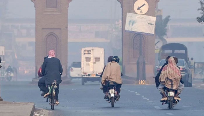 Commuters wrapped in shawls on the road in cold weather in Lahore on December 2, 2024. — AFP