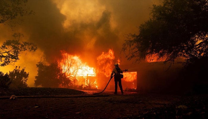 A firefighter tries to control the fire burning down a house as the Mountain Fire scorches acres, the wildfire fueled by strong Santa Ana winds, in Camarillo, California, on November 6, 2024. — AFP