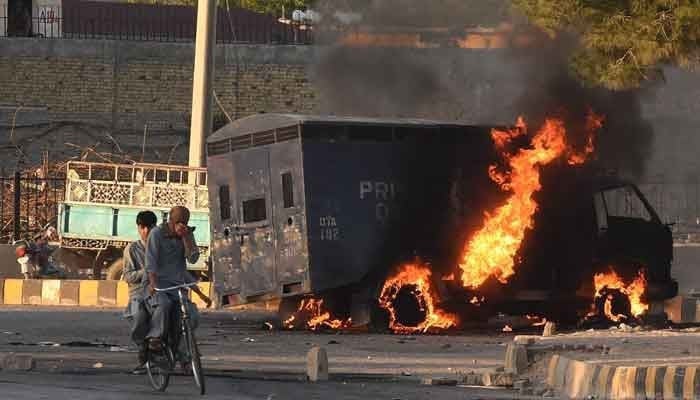 Men on a cycle ride past a burning police vehicle during a protest by Pakistan Tehreek-e-Insaf party activists and supporters of former prime minister Imran against the arrest of their leader, in Quetta on May 9, 2023. —AFP