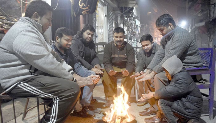 Shopkeepers sit around a bonfire at a local market during a winter night in Lahore on December 30, 2023. — Online