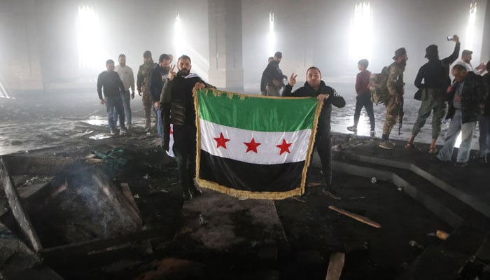 Rebel fighters stand next to the burned gravesite of Syria’s late president Hafez al-Assad at his mausoleum in the family’s ancestral village of Qardaha on December 11, 2024. — AFP