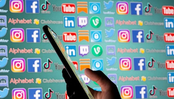 The representational image shows a person holding smartphone in front of displayed social media logos in this illustration taken on May 25, 2021. — Reuters