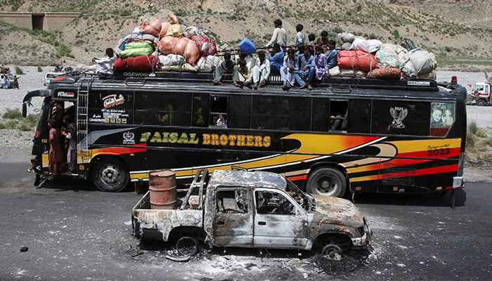 A bus with passengers sitting on the roof with belongings, drives past a damaged vehicle, a day after militants conducted deadly attacks, in Bolan district in Balochistan on August 27, 2024. — Reuters