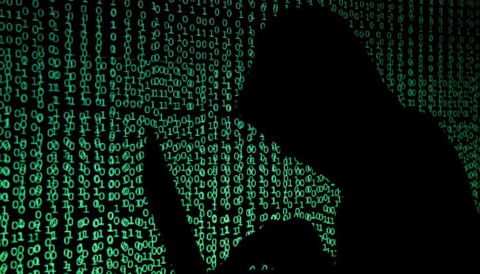 A person wearing a balaclava is silhouetted as he poses with a laptop in front of a screen projected with the word cyber and binary code, in this picture illustration taken in Zenica October 29, 2014. — Reuters