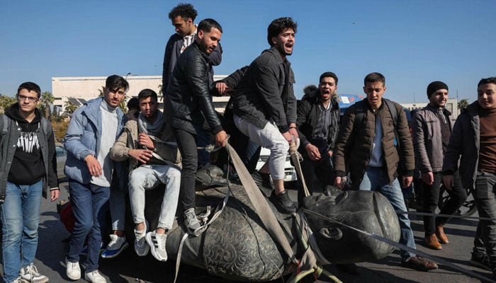 Students stand on the toppled statue of late president Hafez al-Assad during a rally near Damascus University. —AFP/File