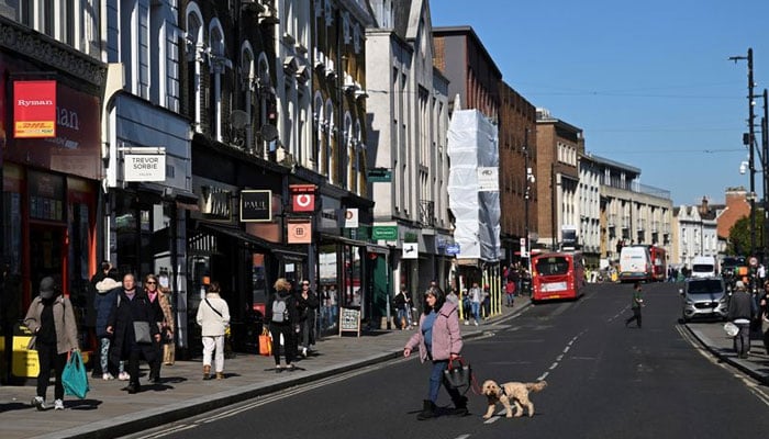 A woman walks across the road with her dog on the high street of Richmond, in London, Britain, October 11, 2024. — Reuters