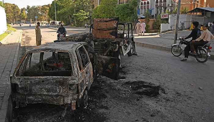 Motorcyclists ride past burnt vehicles in front of the Pakistan Army Institute, a day after protests by Pakistan Tehreek-e-Insaf (PTI) party activists and supporters of former Pakistan´s Prime Minister Imran Khan, in Rawalpindi on May 10, 2023. — AFP