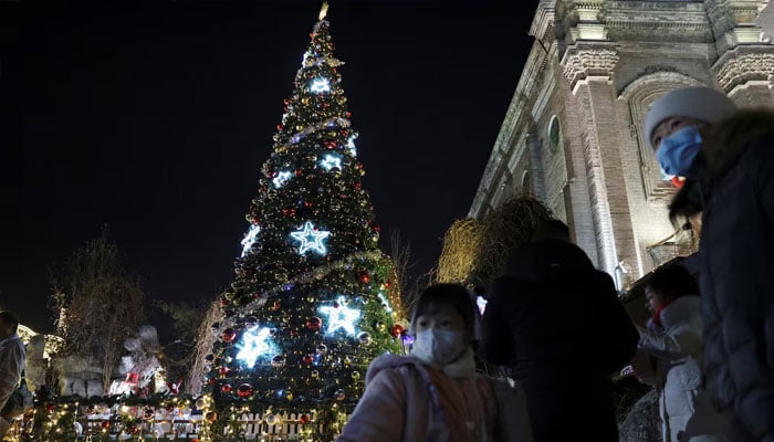 A child holds a toy near a Christmas tree outside the South Cathedral, a Catholic church at Xuanwumen, on Christmas Eve in Beijing, China December 24, 2023. —Reuters