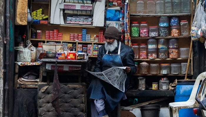 A man reads newspaper while selling betel leaves, known as pan, cigarettes and candies from a shop in Karachi on December 30, 2021. — Reuters