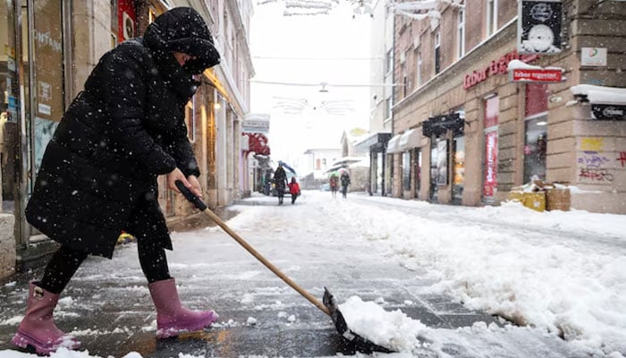 A woman shovels snow on the main street during snowstorm in Sarajevo, Bosnia and Herzegovina, December 24, 2024.— Reuters