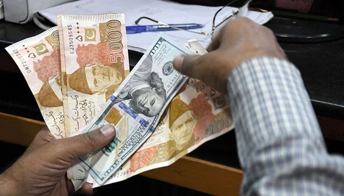 A man counts Pakistani rupee notes and foreign currency at a shop in Karachi, on March 2, 2023. — Online