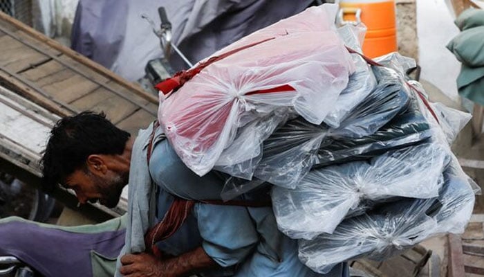 A labourer bends over as he carries packs of textile fabric on his back to deliver to a nearby shop in a market in Karachi on June 24, 2022. — Reuters