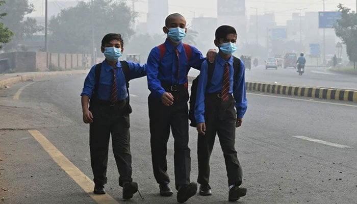 Representational image shows school boys wearing masks as they walk along a road amid heavy smog in Lahore on October 29, 2024. — AFP