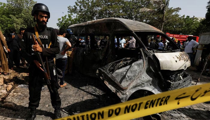 A police officer stands guard near a passenger van, cordoned after a blast at the entrance of the Confucius Institute University of Karachi on April 26, 2022. — Reuters