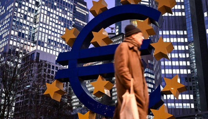 A person passing by a euro sign. — AFP/File