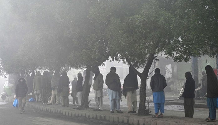 Labourers working on daily wages stand along the roadside before being hired by people on a foggy winter morning in Lahore on January 2, 2025. — AFP