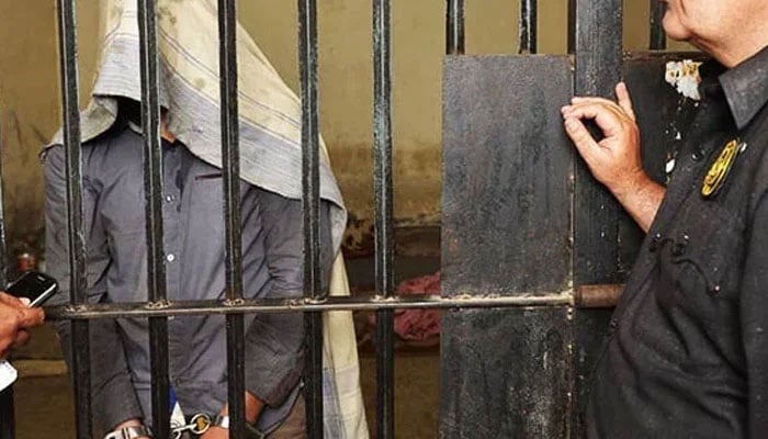 The representational image shows a handcuffed man standing behind bars with a policeman standing outside the jail. — AFP/File