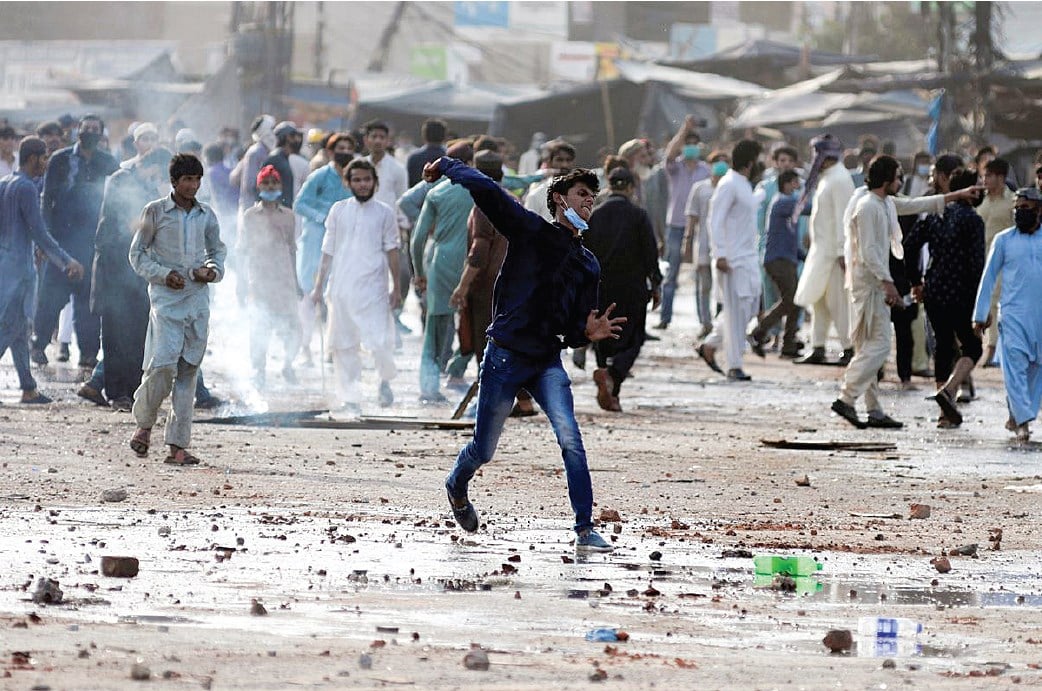A supporter of the Tehreek-e-Labaik Pakistan (TLP) hurls stones towards police during a protest in Lahore. Image courtesy: Reuters