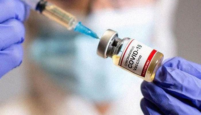 A woman holds a small bottle — labeled Coronavirus COVID-19 Vaccine — and a medical syringe. Photo: file