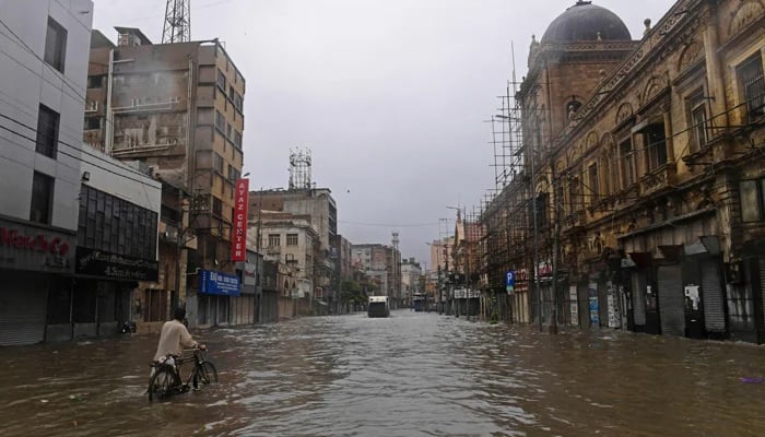 A commuter makes his way through a flooded street after heavy rain showers in Karachi on July 11, 2022. -AFP