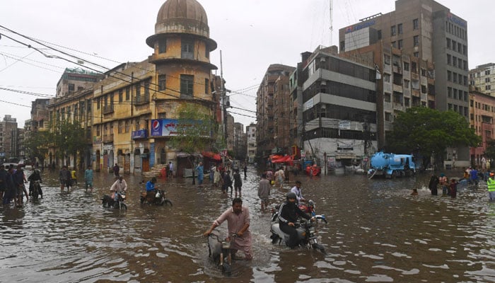 People wade across a flooded street after heavy monsoon rainfall in Karachi on July 25, 2022. Photo: AFP