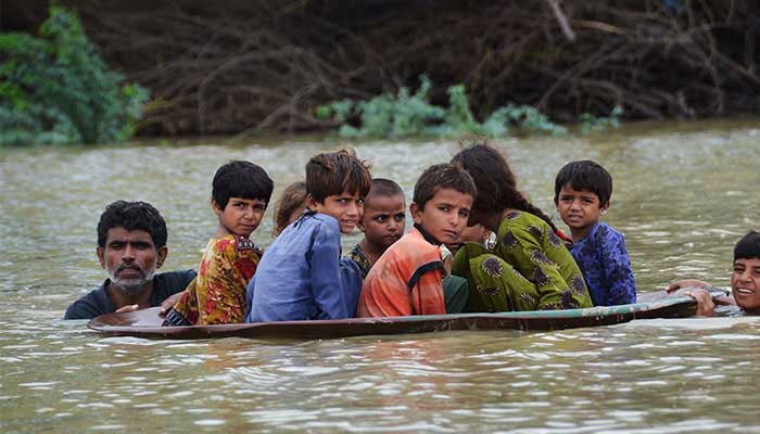 A man along with a youth use a satellite dish to move children across a flooded area in Balochistan. Photo: AFP/file