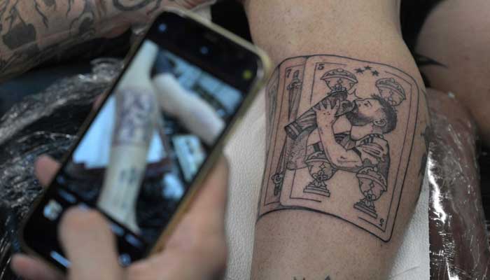 Argentine tattooist Tebi Cobra Vucinovich takes a photo of the tattoo of Argentina´s world champion Lionel Messi kissing the FIFA World Cup trophy on the leg of Ariel Sacchi at Ds Tattoo Shop in Buenos Aires on December 23, 2022. — AFP
