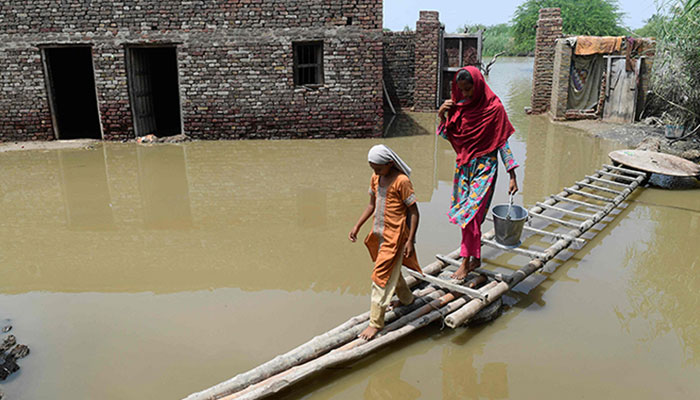 Flood-affected people walk on a temporary bamboo path near their flooded house in Shikarpur of Sindh province on August 29, 2022. — AFP