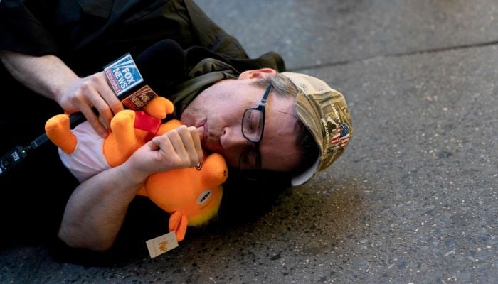 A person impersonating a Fox News host, lies on the ground holding a stuffed pig in the likeness of former US President Donald Trump, near Trump Tower in New York City on April 3, 2023.— AFP