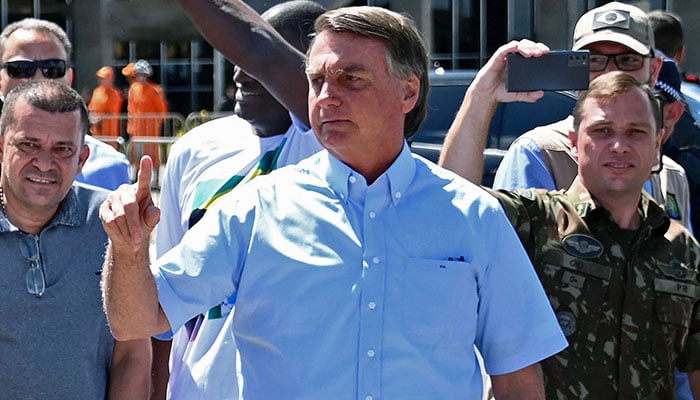 (FILES) Brazilian President Jair Bolsonaro (C), accompanied by personal assistant army officer Mauro Cid (R), greets supporters cheering for him and his controversial ally, deputy Daniel Silveira, who Bolsonaro pardoned after the Supreme Court had sentenced him to prison time for his role leading a movement calling for the court to be overthrown, in Brasilia on May Day, on May 1, 2022.—AFP