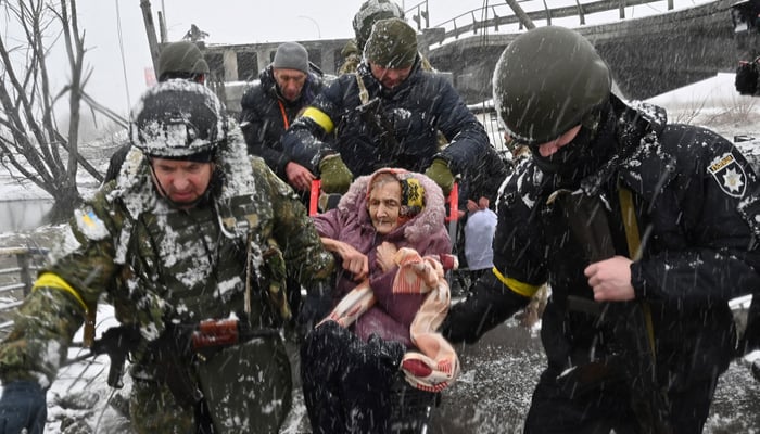 Ukrainian soldiers help an elderly woman to cross a destroyed bridge as she evacuates the city of Irpin, northwest of Kyiv. — AFP