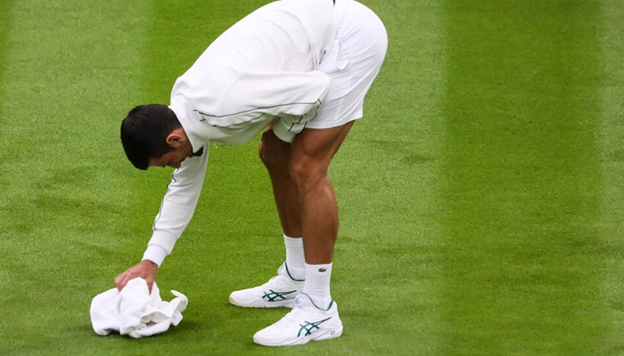 Serbias Novak Djokovic helps to dry Wimbledons Centre Court. — AFP