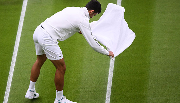 Serbia´s Novak Djokovic jokes as he attempts to dry the grass of Center Court with a towel as the rains starts to fall during his men´s singles tennis match against Argentina´s Pedro Cachin on the first day of the 2023 Wimbledon Championships at The All England Tennis Club in Wimbledon, southwest London, on July 3, 2023.—AFP