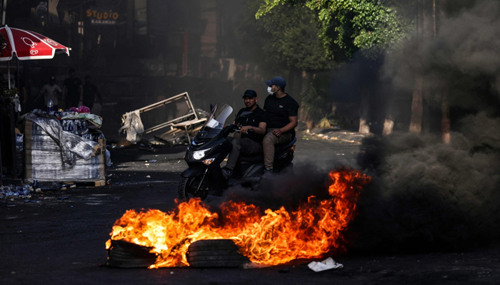 Men ride a motorcycle past a fire amidst clashes between Palestinians and the Israeli army in the occupied West Bank city of Jenin on July 4, 2023. — AFP