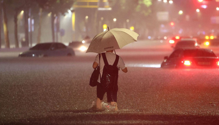 A man wades alongside submerged cars in a street during heavy rainfall in the Gangnam district of Seoul, South Korea, on August 8, 2022. — AFP