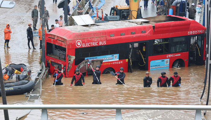 South Korean rescue workers search for missing persons near a bus along a deluged road leading to an underground tunnel where some 15 cars were trapped in flood waters after heavy rains in Cheongju on July 16, 2023. — AFP