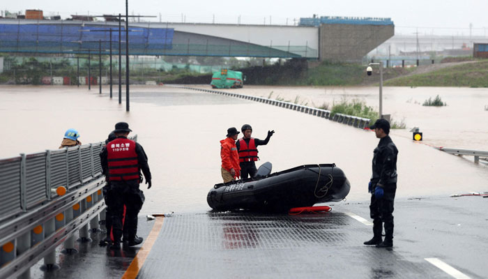 South Korean emergency workers search for survivors on a flooded road leading to an underground tunnel where some 19 cars were trapped by flood waters after heavy rains in Cheongju on July 15, 2023. — AFP